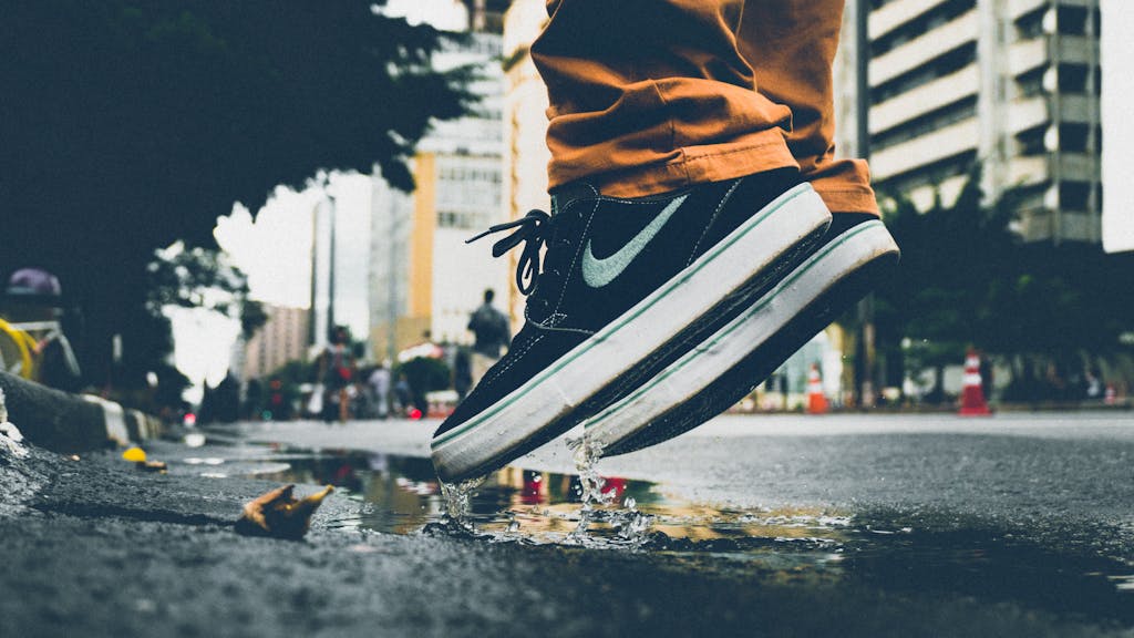 Close-up of sneakers splashing water in an urban street scene, capturing motion and reflection.