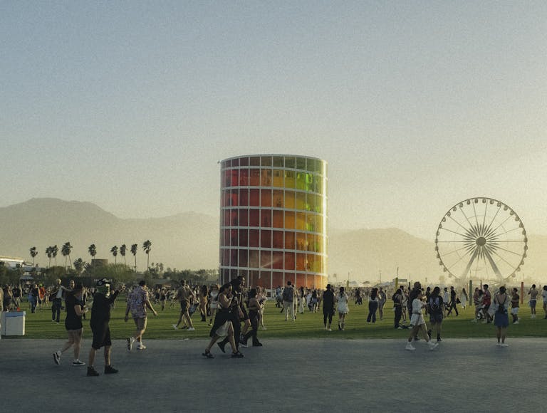 People enjoying a lively music festival with a colorful tower and Ferris wheel backdrop.